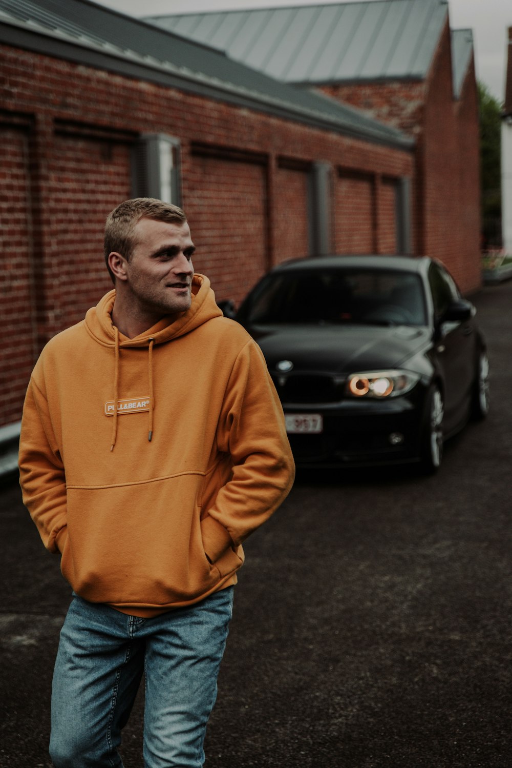 man in brown hoodie standing near black car during daytime