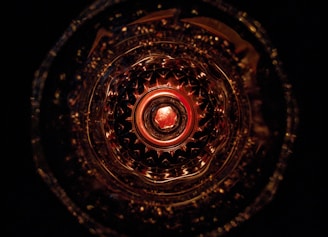 An intricate and symmetrical pattern viewed from a top perspective, resembling a kaleidoscope effect with a central circular motif. The pattern is illuminated in warm tones, creating a sense of depth and complexity.