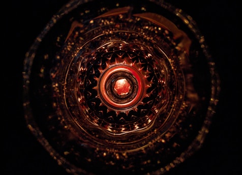 An intricate and symmetrical pattern viewed from a top perspective, resembling a kaleidoscope effect with a central circular motif. The pattern is illuminated in warm tones, creating a sense of depth and complexity.