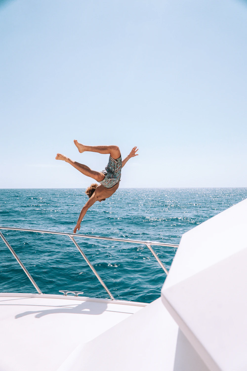 A man diving off the bow of a white yacht into the sea