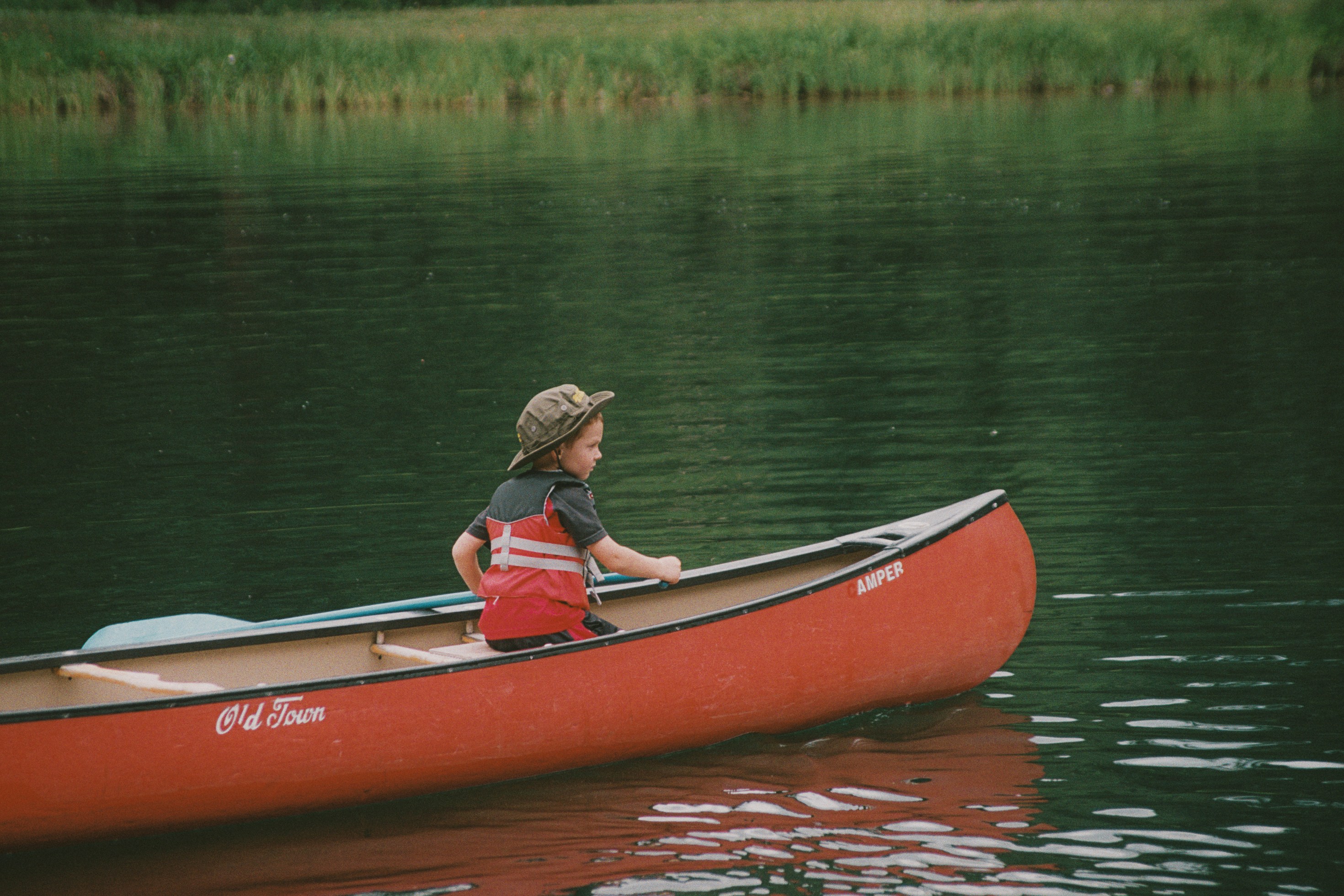 Mujer con chaleco rojo montando kayak rojo en el lago durante el día