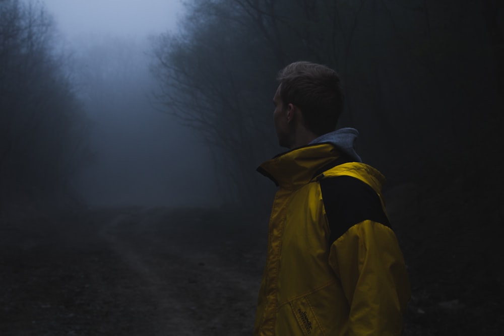 man in yellow jacket standing near green trees during daytime