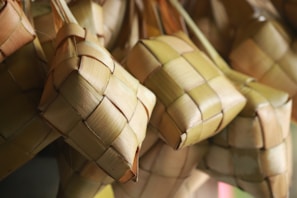 Handwoven palm leaves in a geometric pattern form small, square pouches. The texture is smooth, and the colors vary from light beige to soft green.