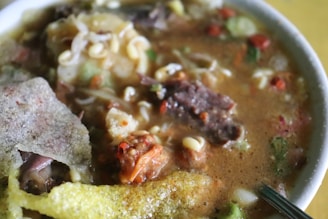 A close-up of a steaming bowl of hearty vegetable soup.