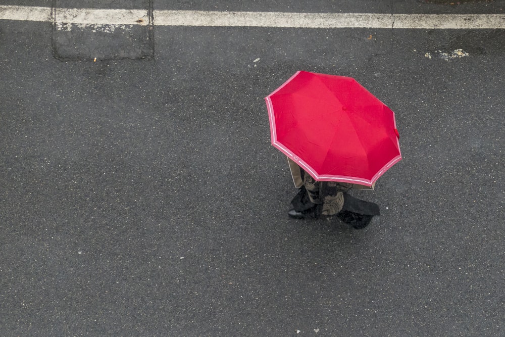 昼間、灰色のアスファルト道路を歩く赤い傘をさした人