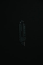 A black utility knife with a visible metal blade is placed upright against a dark background, highlighting its sleek and modern design.