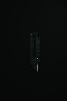 A black utility knife with a visible metal blade is placed upright against a dark background, highlighting its sleek and modern design.