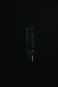 A black utility knife with a visible metal blade is placed upright against a dark background, highlighting its sleek and modern design.