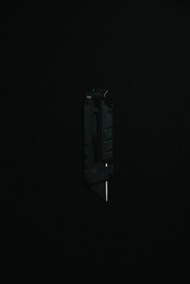 A black utility knife with a visible metal blade is placed upright against a dark background, highlighting its sleek and modern design.