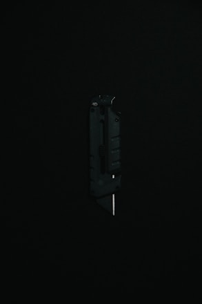 A black utility knife with a visible metal blade is placed upright against a dark background, highlighting its sleek and modern design.