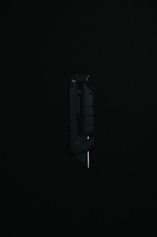 Top-down shot of a black tactical knife with a clean design, displayed against a solid black surface enhancing its sleek look.