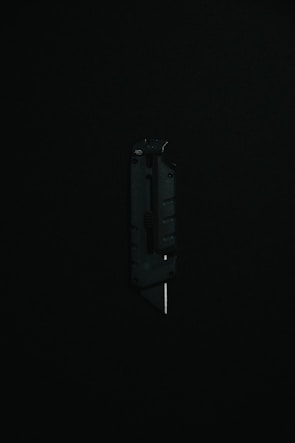 A black utility knife with a visible metal blade is placed upright against a dark background, highlighting its sleek and modern design.