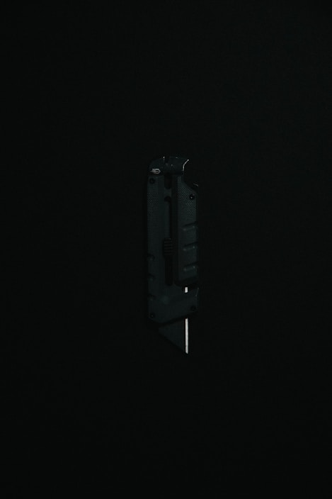 A black utility knife with a visible metal blade is placed upright against a dark background, highlighting its sleek and modern design.