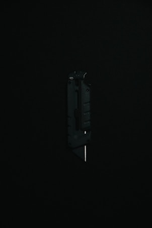 A black utility knife with a visible metal blade is placed upright against a dark background, highlighting its sleek and modern design.