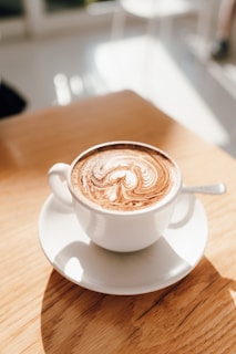 A steaming cappuccino with delicate latte art served in a ceramic cup on a sunlit café table.
