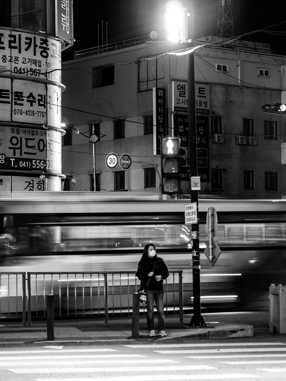 grayscale photo of woman in black jacket standing on sidewalk