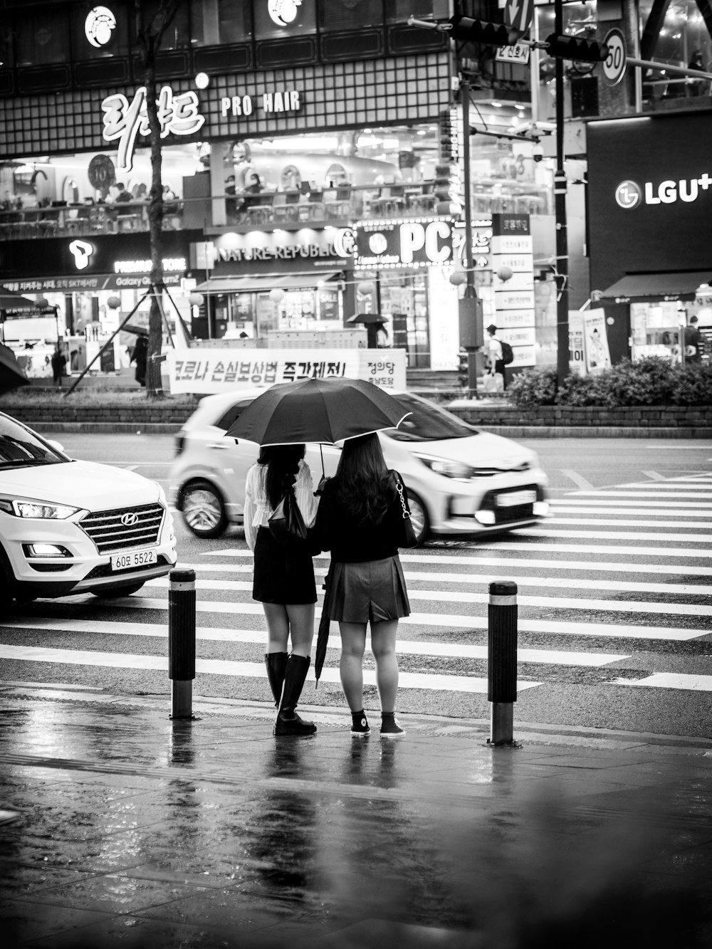 grayscale photo of man and woman holding umbrella walking on pedestrian lane
