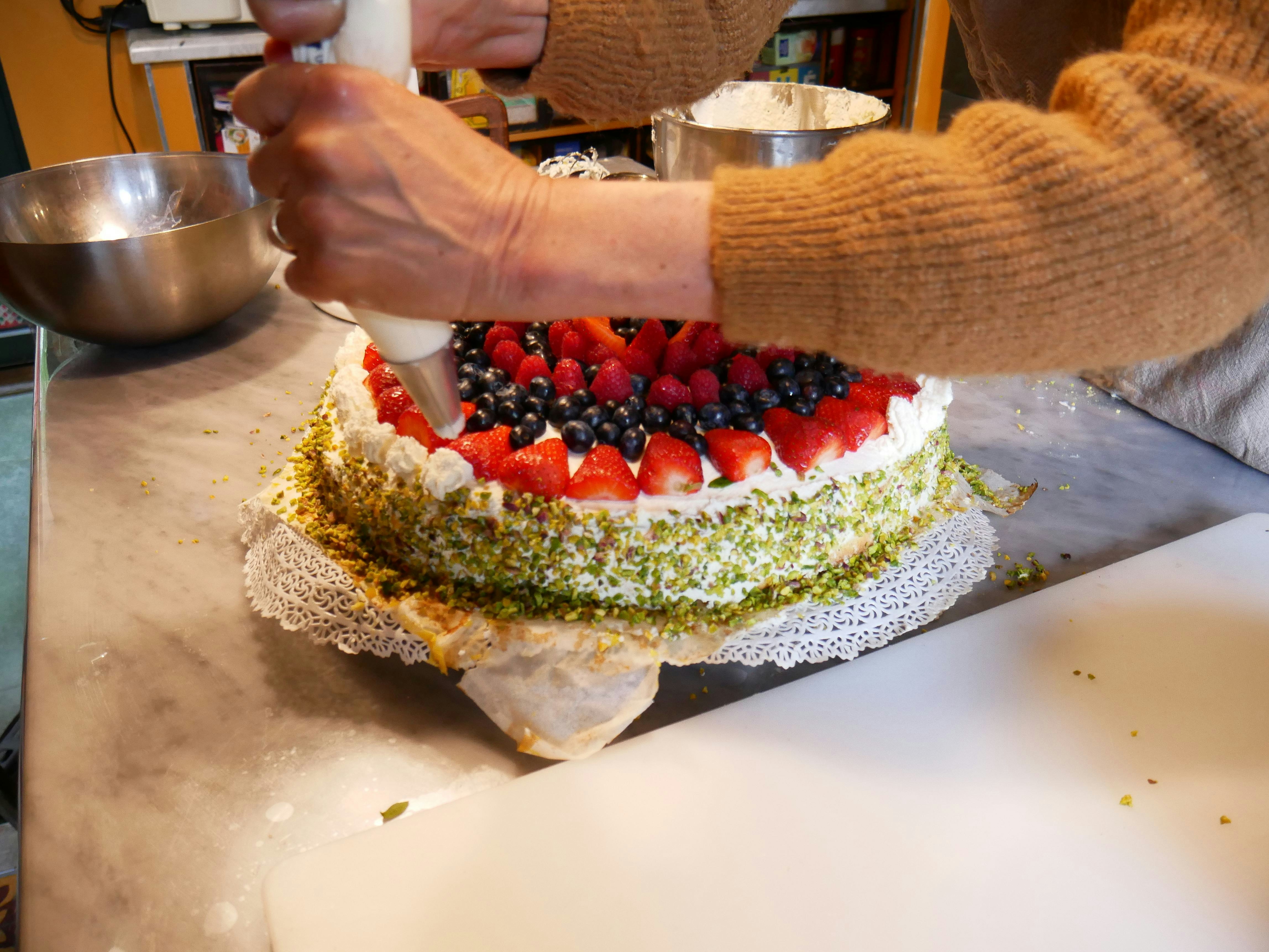 Artisan pastry chef hands carefully piping cream decorations on a layered chocolate cake in professional kitchen