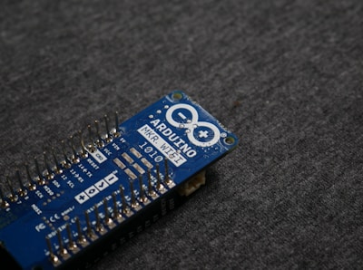 A blue Arduino MKR WiFi 1010 microcontroller board placed on a gray fabric surface. The board features numerous metal pins along one side and is marked with white text identifying its model and specifications.