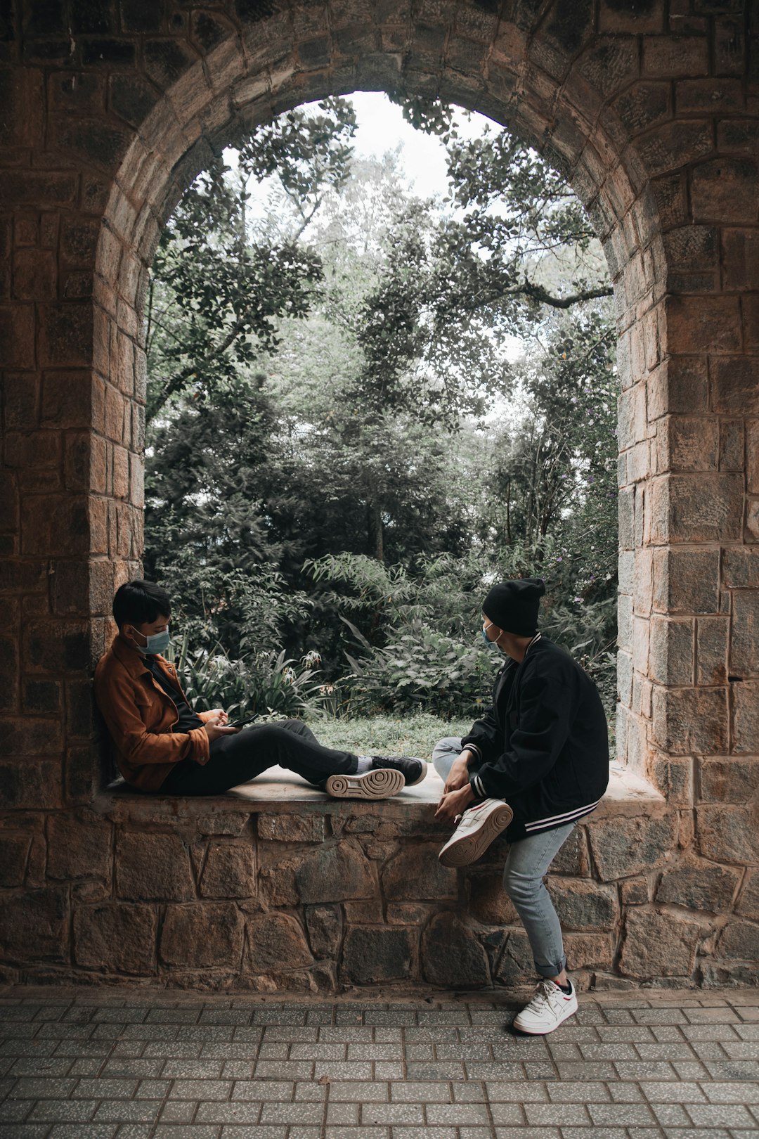 man in black jacket and black pants sitting on brown concrete wall during daytime