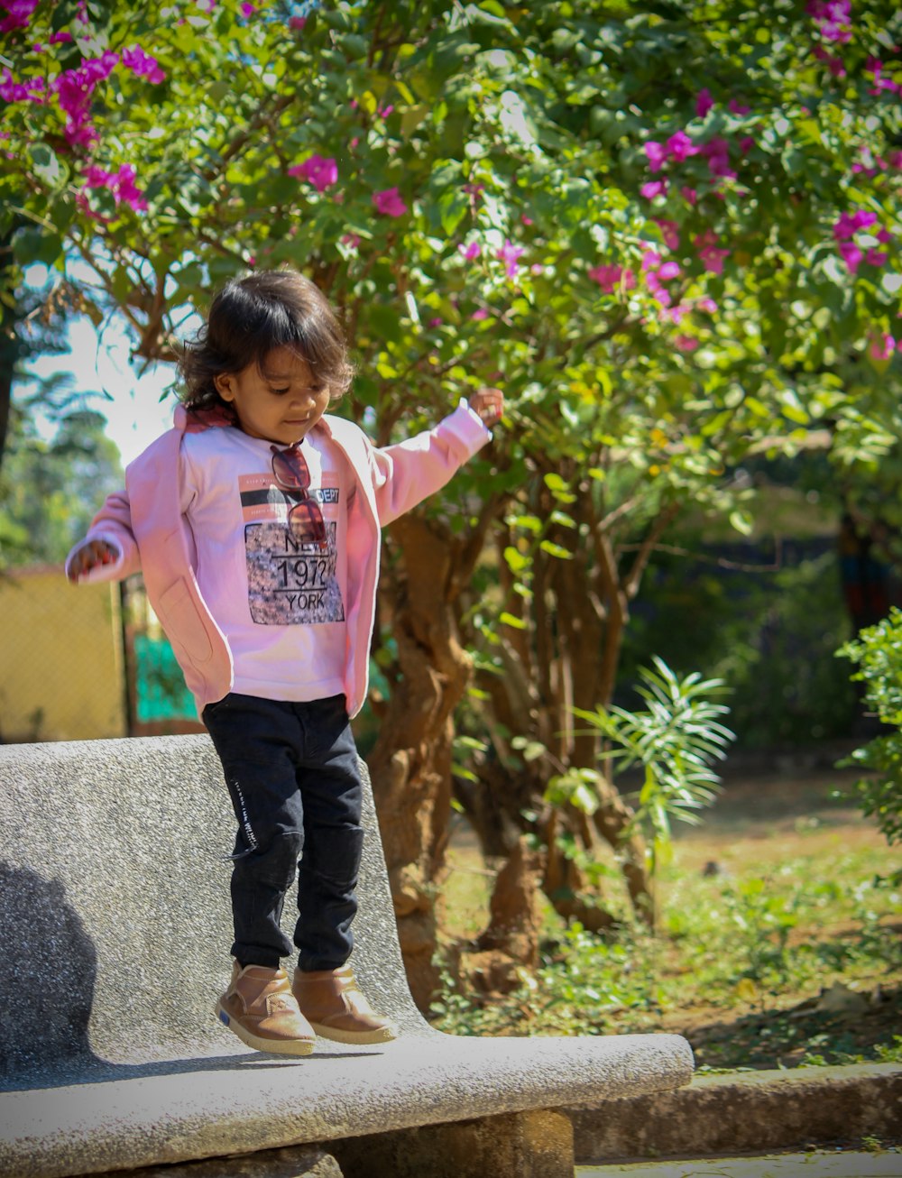 girl in pink long sleeve shirt and black pants standing on gray concrete pathway during daytime