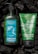 Two Bath & Body Works aromatherapy products featuring stress relief properties are placed against a dark background. The left product is a green bottle of moisturizing body lotion infused with eucalyptus and tea, adorned with water droplets. On the right is a green tube of invigorating body scrub with eucalyptus and spearmint. Both products are surrounded by pieces of black charcoal.