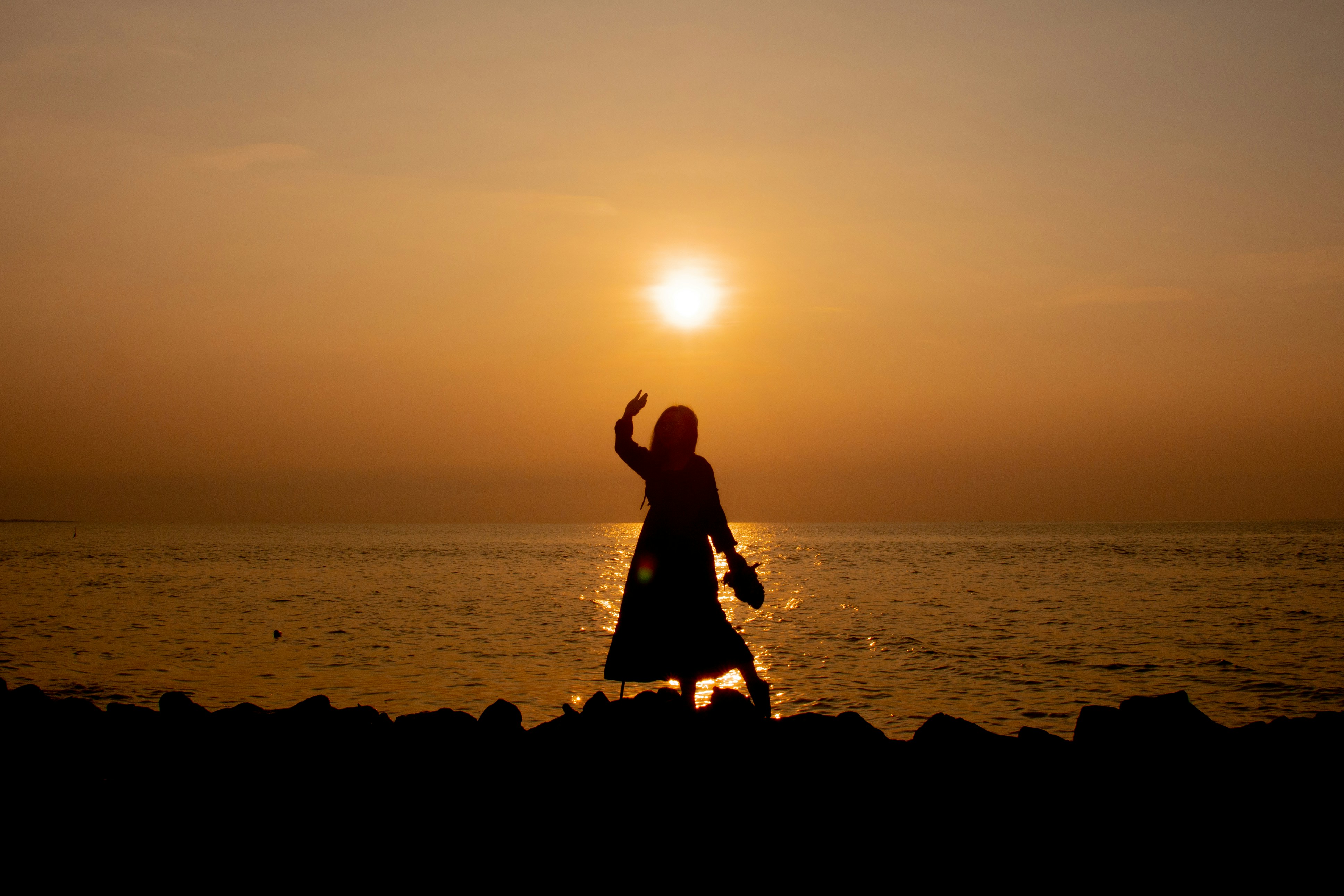 silhouette of 2 women standing on rock formation near body of water during sunset