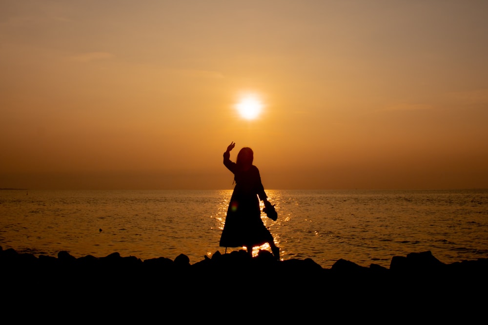 silhouette of 2 women standing on rock formation near body of water during sunset