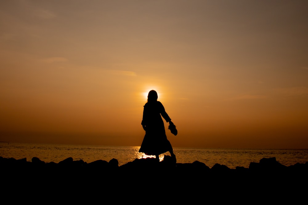 silhouette of man and woman standing on rock near body of water during sunset