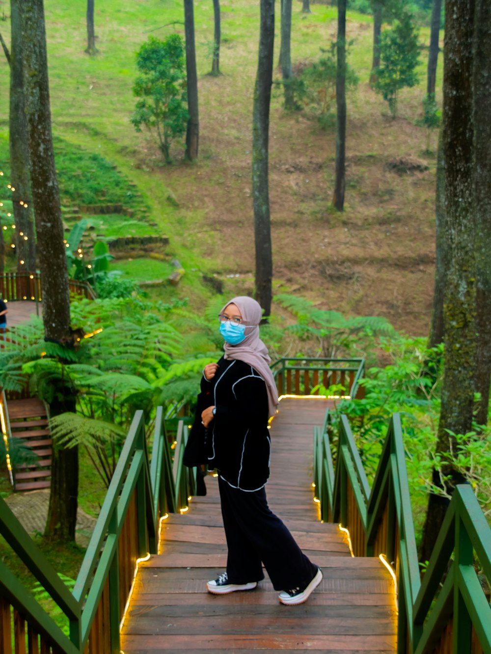 woman in black long sleeve shirt walking on wooden bridge