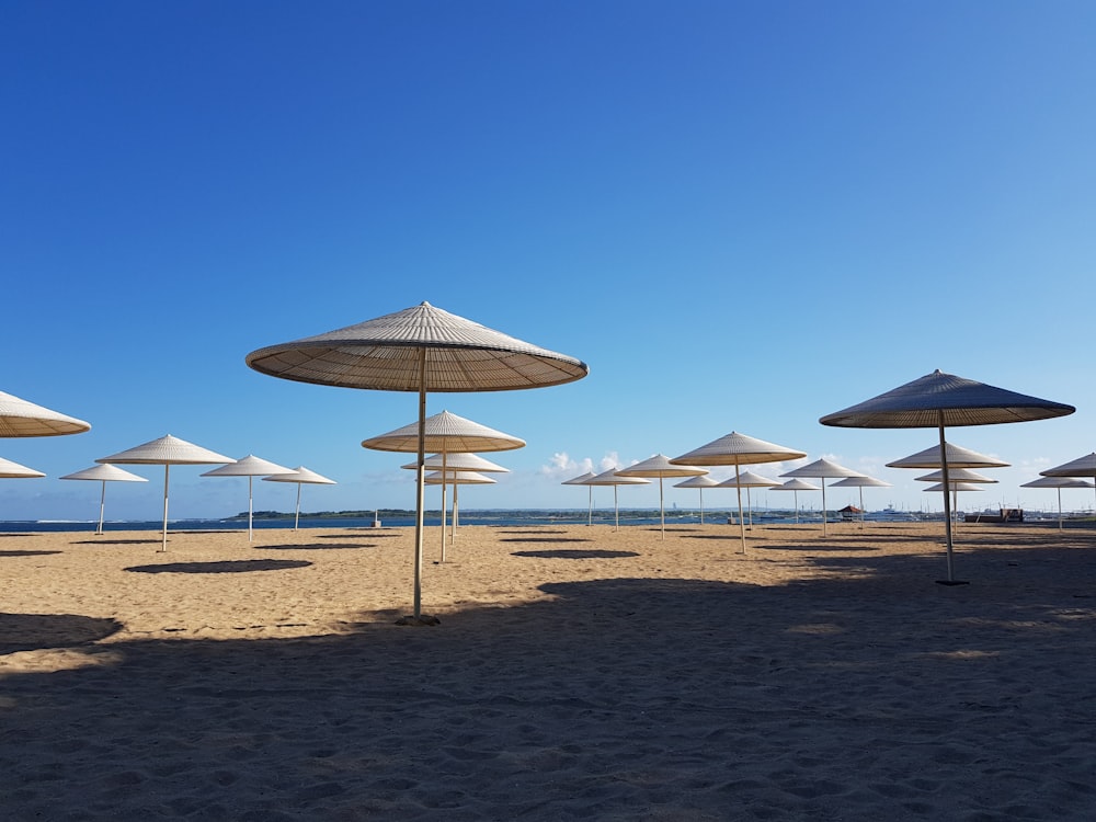 ombrelloni bianchi e marroni su sabbia marrone sotto il cielo blu durante il giorno