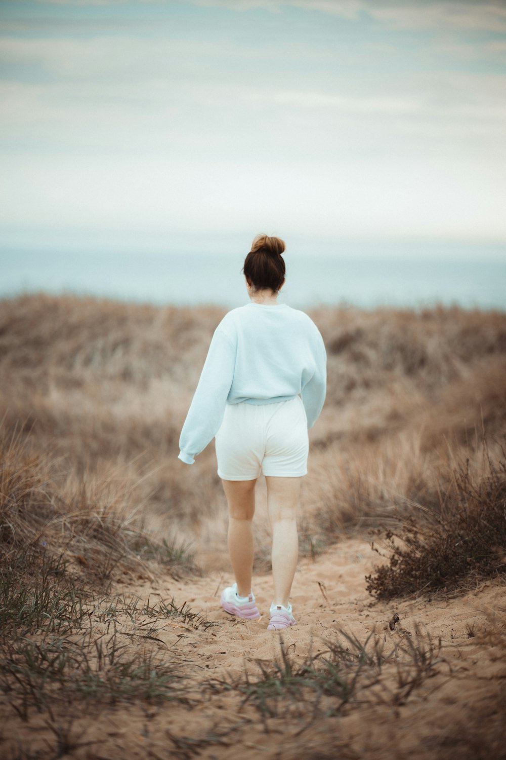 woman in white long sleeve shirt walking on brown dirt road during daytime