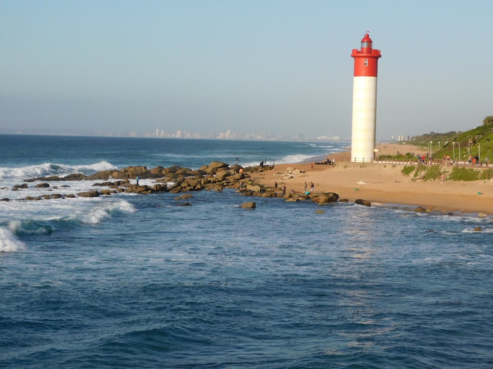 Faro blanco y rojo en arena marrón cerca del cuerpo de agua durante el día