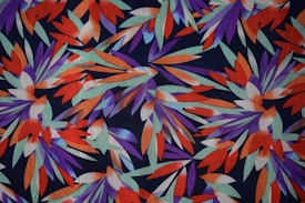 A vibrant pattern composed of stylized leaf-like shapes. The design features overlapping elements in bold colors such as purple, orange, and teal, creating a dynamic and energetic visual effect.