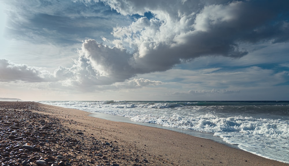 sea waves crashing on shore under cloudy sky during daytime