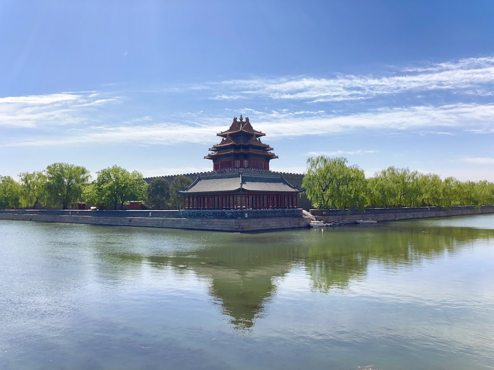brown and green temple near green trees and body of water under blue sky during daytime