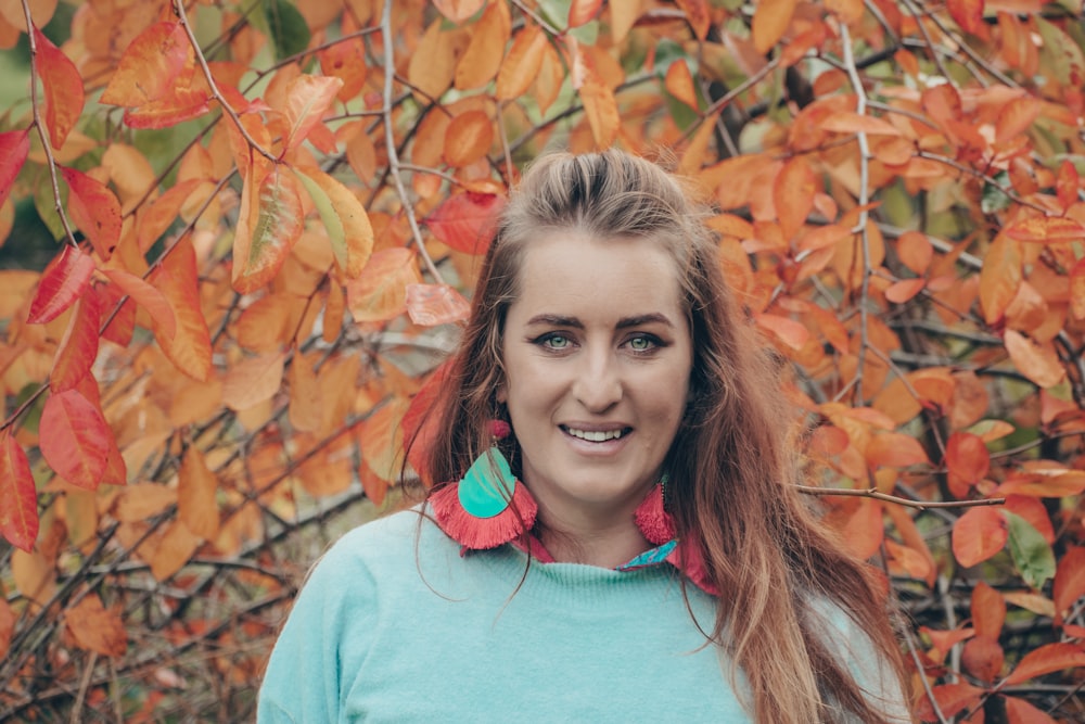 woman in teal crew neck shirt standing near brown leaves during daytime