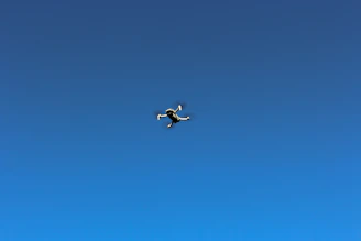 A friendly drone enthusiast flying a small quadcopter against a bright baby blue sky background.