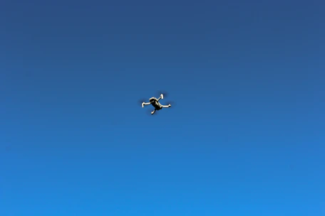 Close-up of a sleek drone hovering outdoors against a clear blue sky.