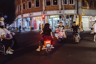 A vibrant cityscape with velloup cars and scooters moving swiftly along illuminated streets at night.