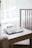 A workspace setting is depicted with a white table and a wooden chair. On the table lies an open notebook with photos and a paper clip, alongside a closed black notebook and a pen. Soft natural light filters through white curtains, creating a serene atmosphere.