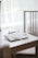 A workspace setting is depicted with a white table and a wooden chair. On the table lies an open notebook with photos and a paper clip, alongside a closed black notebook and a pen. Soft natural light filters through white curtains, creating a serene atmosphere.