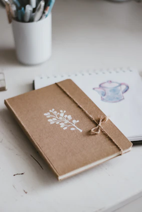 A pastel-colored artistic notebook with impressionist cover design lying open on a wooden desk.
