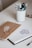 A neatly arranged desk includes a brown notebook with a simple white floral design and a spiral-bound sketchbook open to a page featuring a teapot sketch. Several pens and pencils are organized in a white cup, adding to the creative atmosphere.