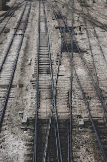 A complex network of railway tracks interwoven with multiple switches and crossings, showing an intricate pattern of parallel steel rails on wooden ties. The surface is covered with gravel and stones, with mechanical components and signs visible alongside the tracks.