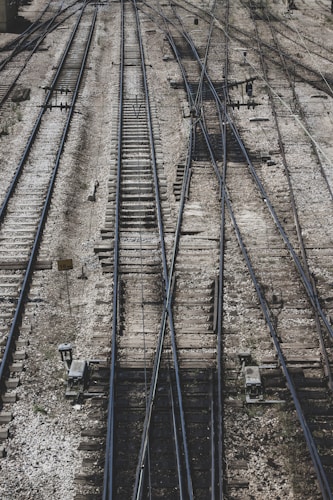 A complex network of railway tracks interwoven with multiple switches and crossings, showing an intricate pattern of parallel steel rails on wooden ties. The surface is covered with gravel and stones, with mechanical components and signs visible alongside the tracks.