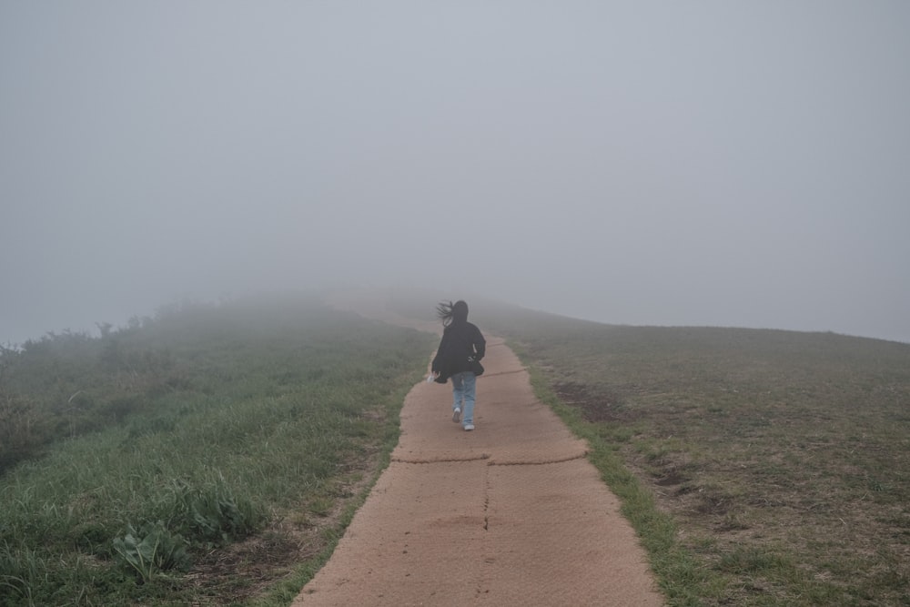 man in black jacket and blue denim jeans walking on brown pathway between green grass field