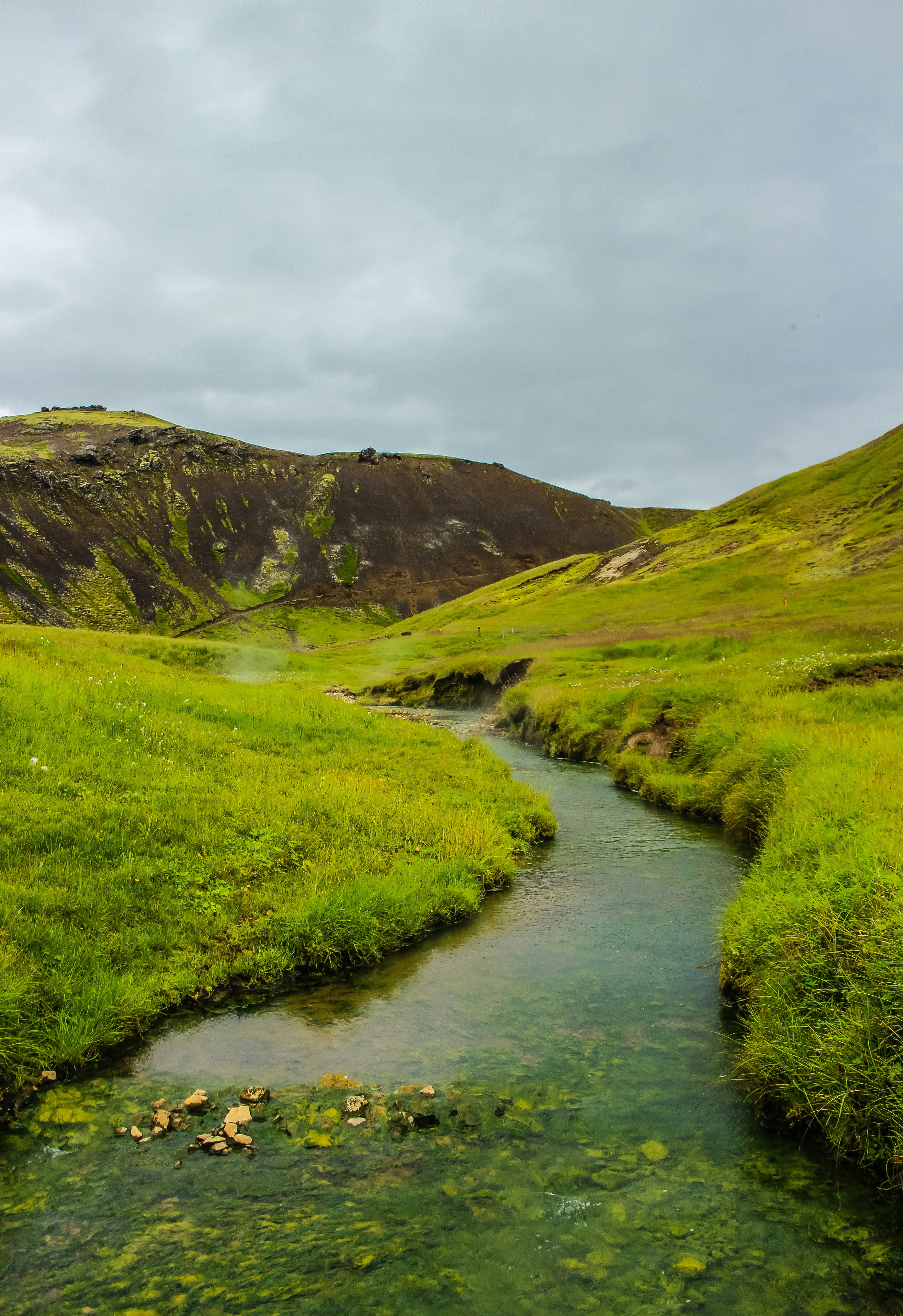 green grass field near river under cloudy sky during daytime