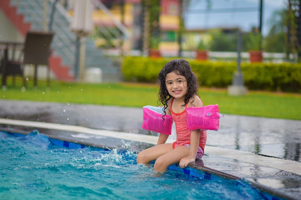 menina na camisa rosa sentada na piscina azul durante o dia