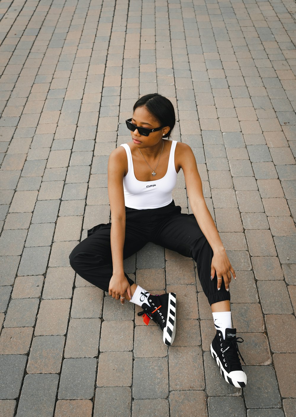 woman in white tank top and black shorts sitting on gray concrete floor